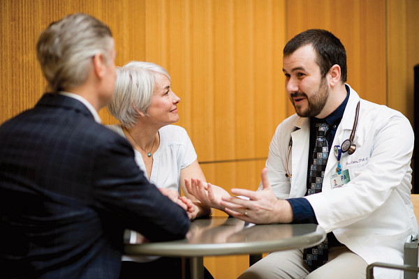 Adult male doctor sitting at table with mature couple.