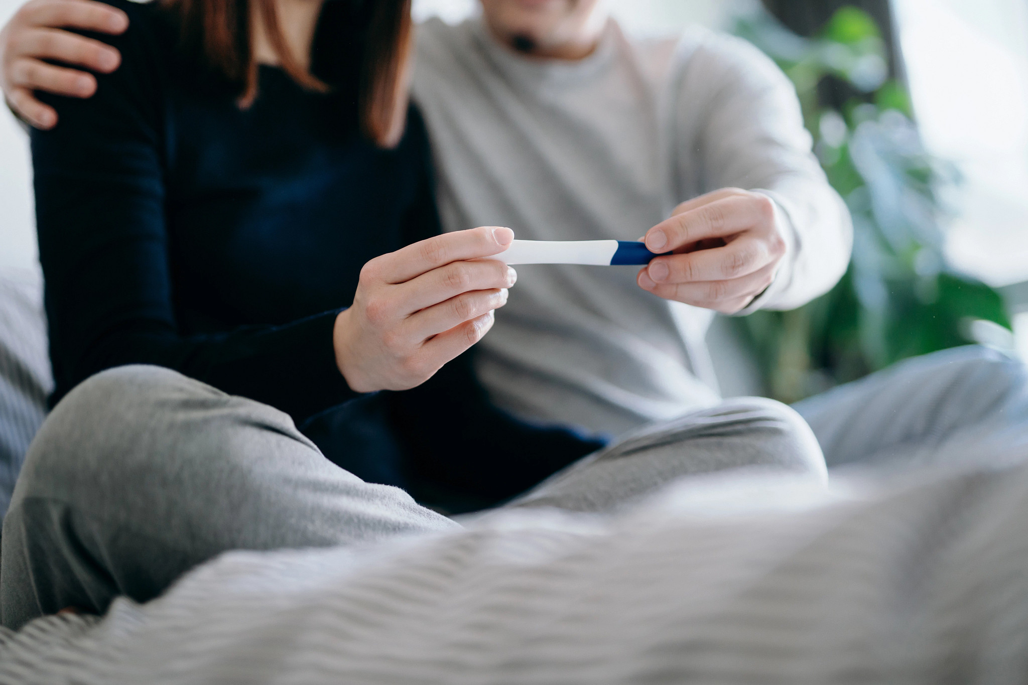 Couple sitting on the bed holding a pregnancy test together