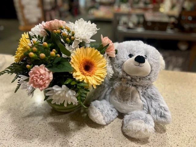 Flowers and plush teddy bear on gift shop counter.