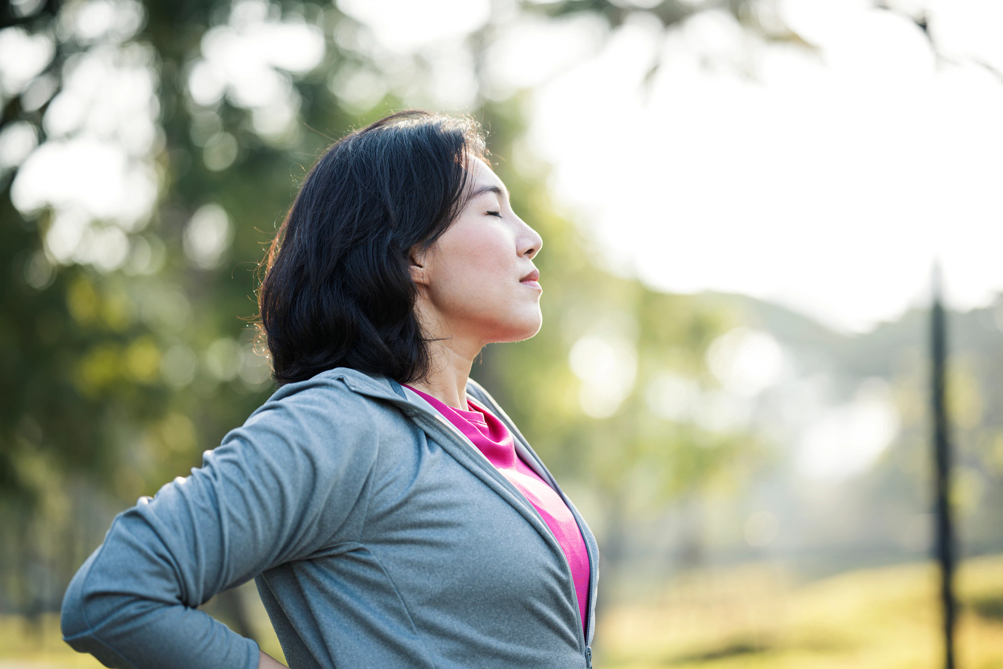 Rest and Recovery After Exercise. Side View of Asian working women take a rest after outdoors workout in a city park.