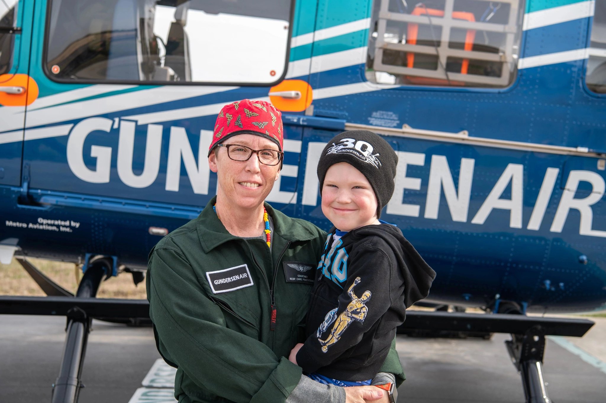 Emplify Health respiratory therapist holding her son in front of medical helicopter.