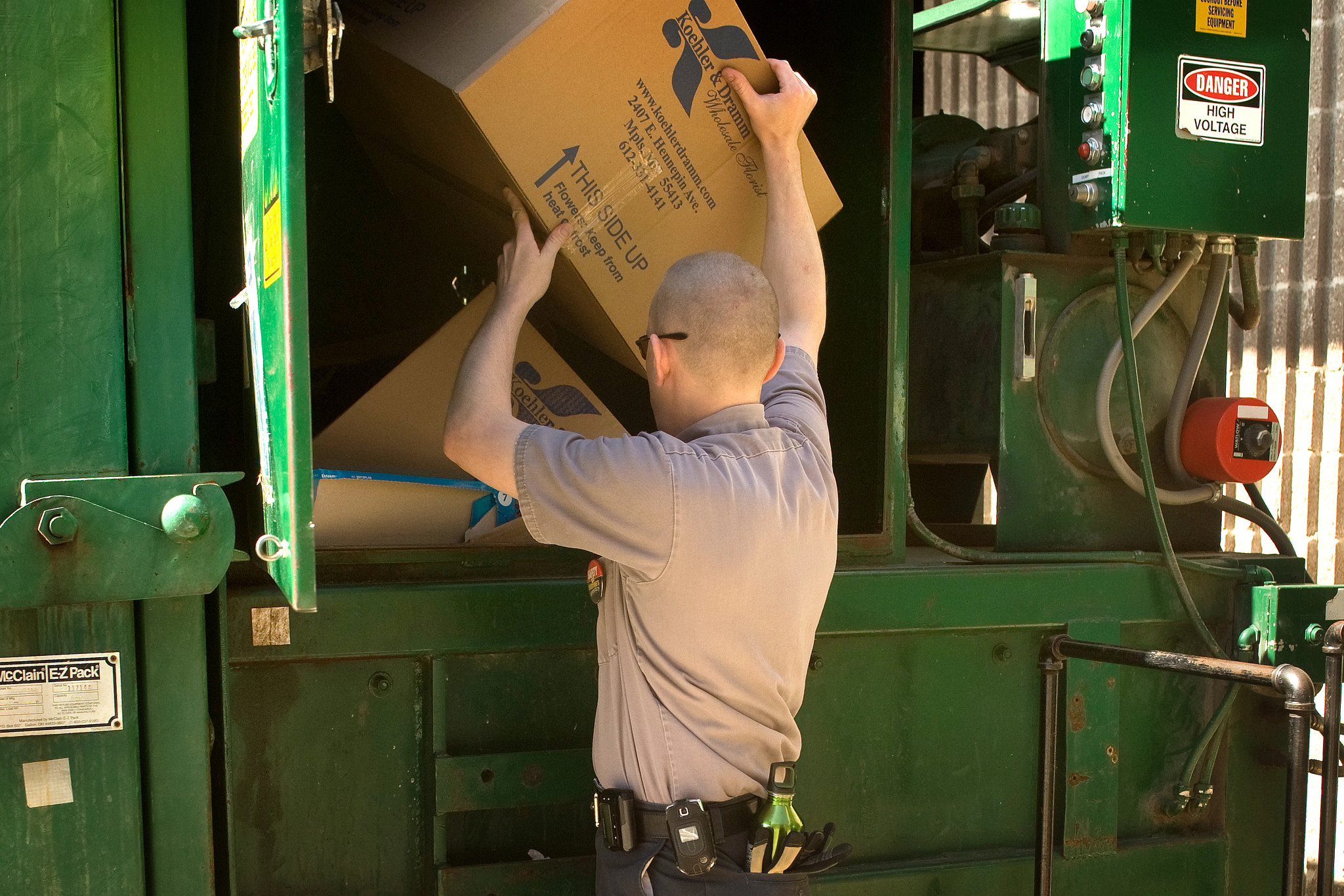 Employee putting cardboard boxes in recycling dumpster.