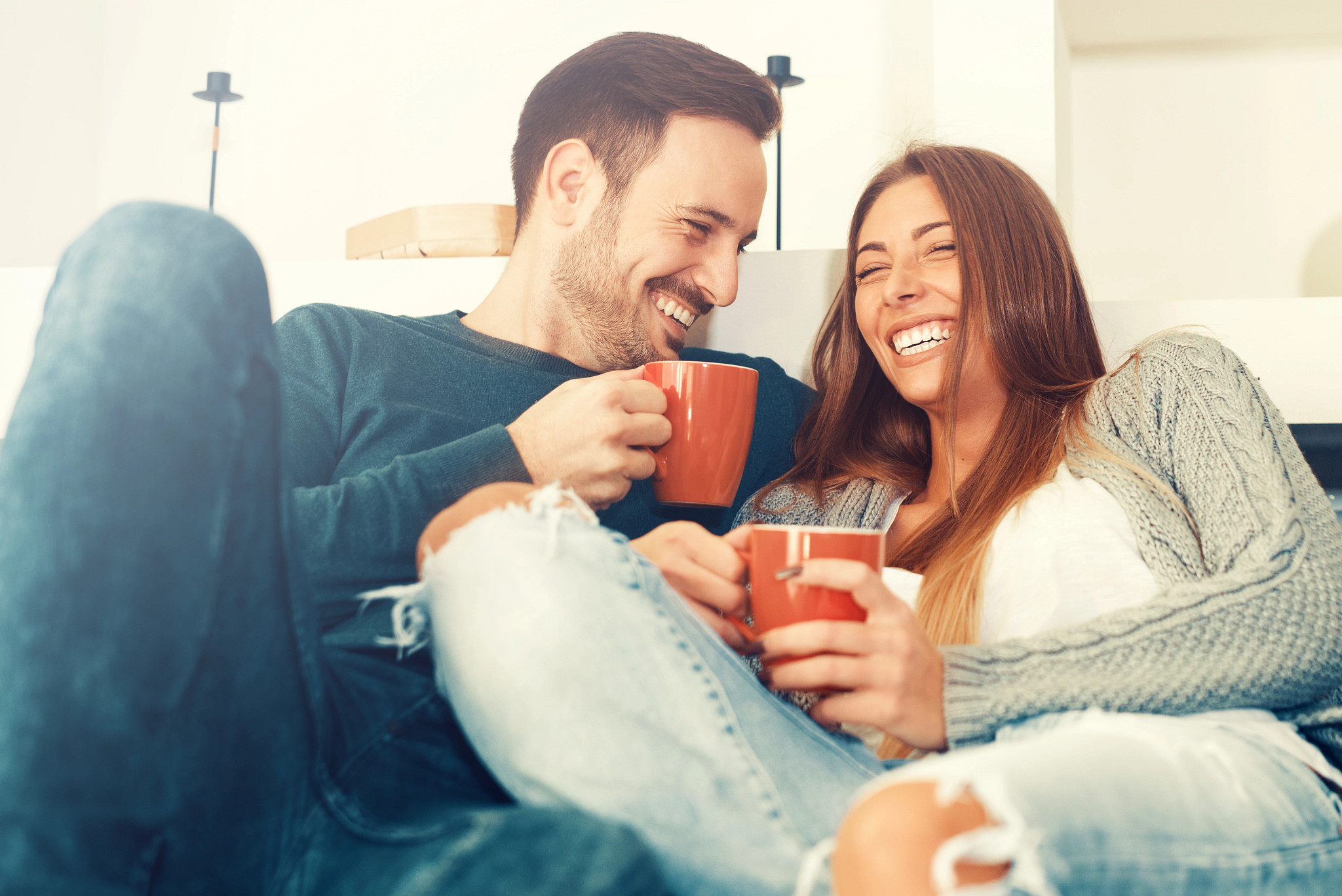 Couple seated on couch enjoying a cup of coffee together.