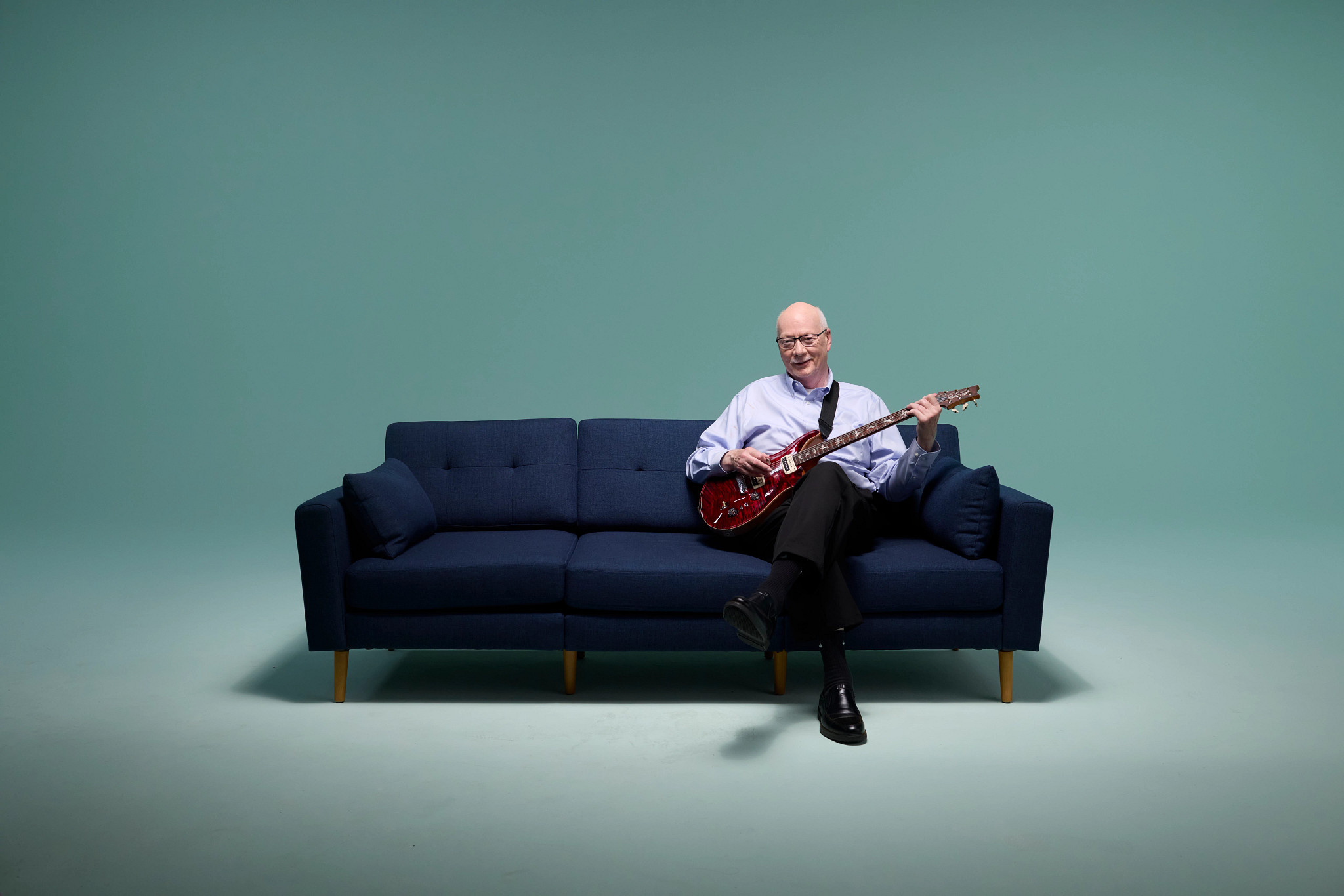 Navy couch on mint background with patient Peter and his guitar.