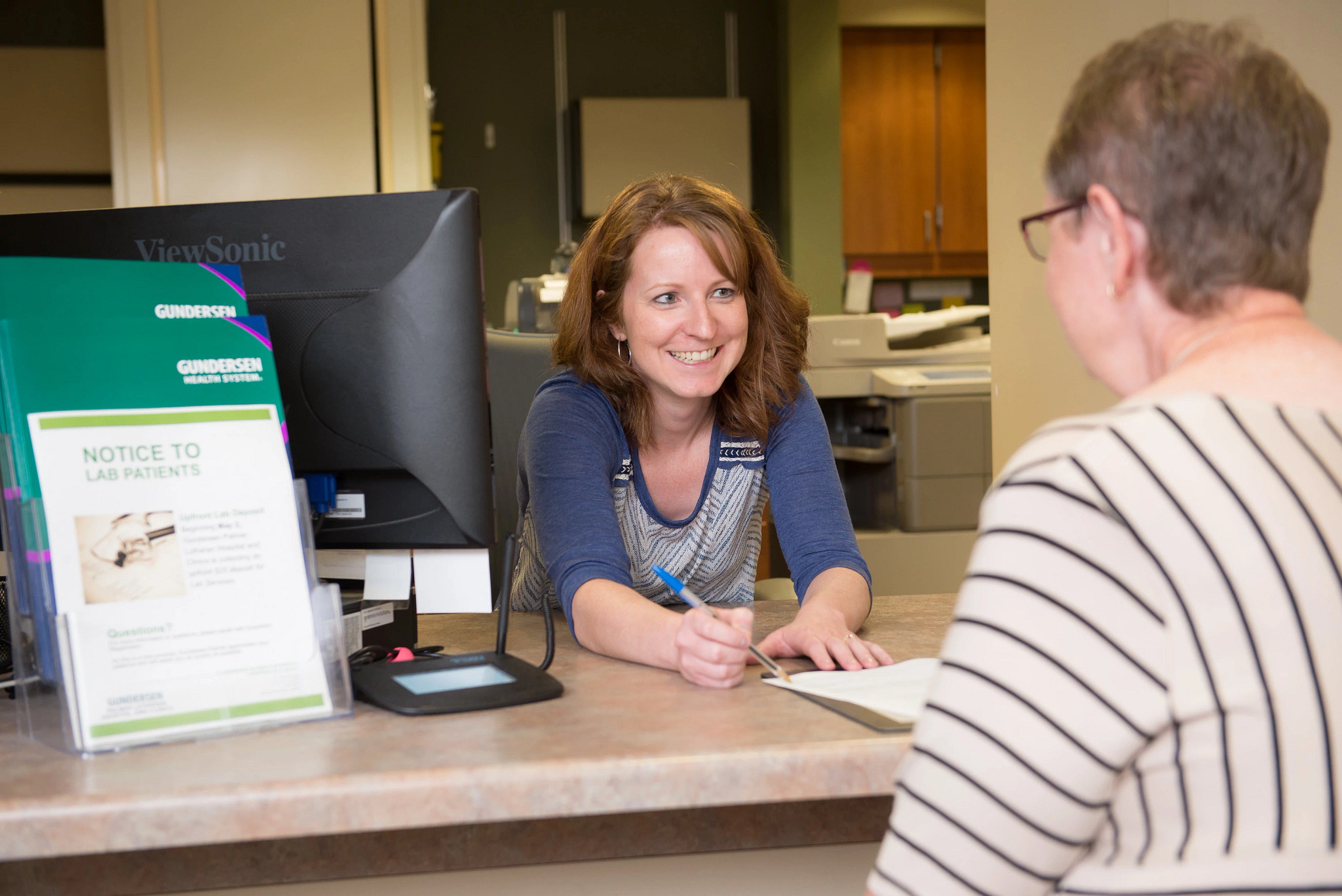 Healthcare receptionist greeting patient at front desk.