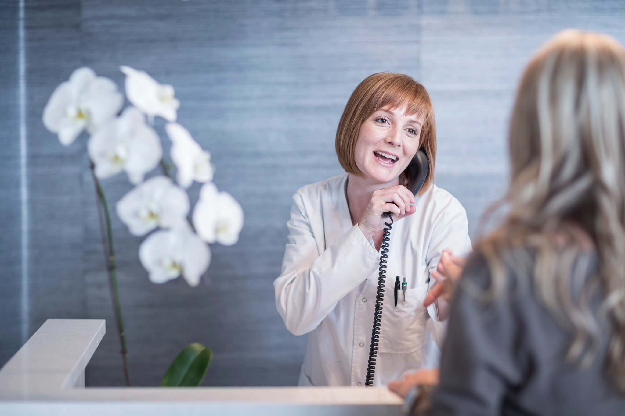 Receptionist greeting patient while on the phone.