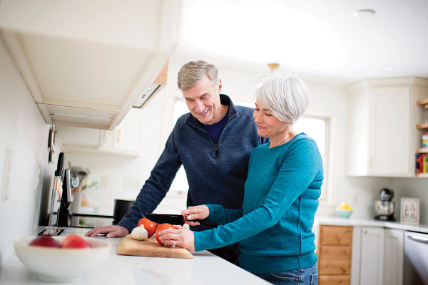 Senior couple cutting up vegetables at kitchen counter.