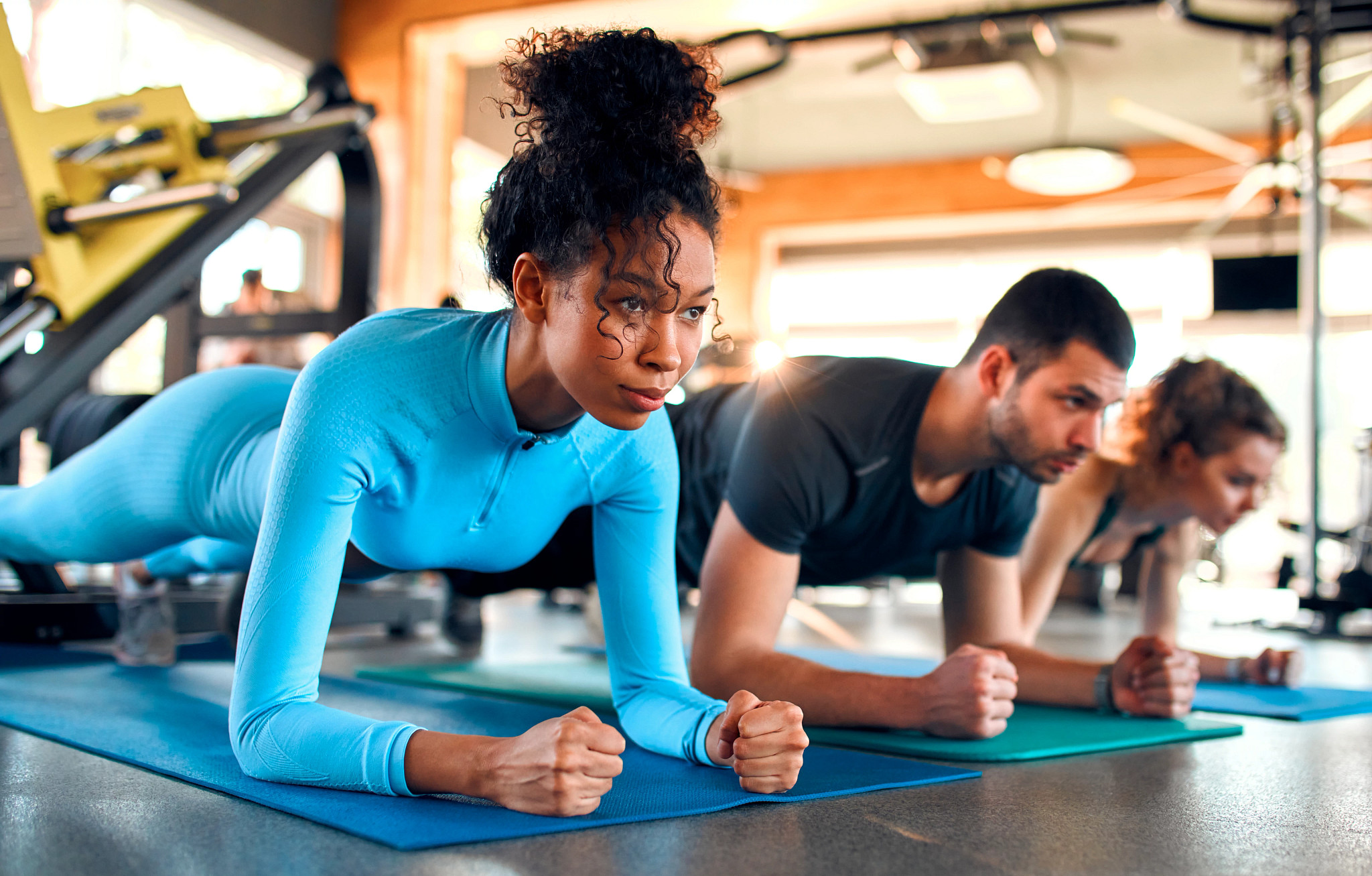 Slim women african american and caucasian ethnicity and muscular man in sportswear doing plank exercise on rubber mat in gym club.