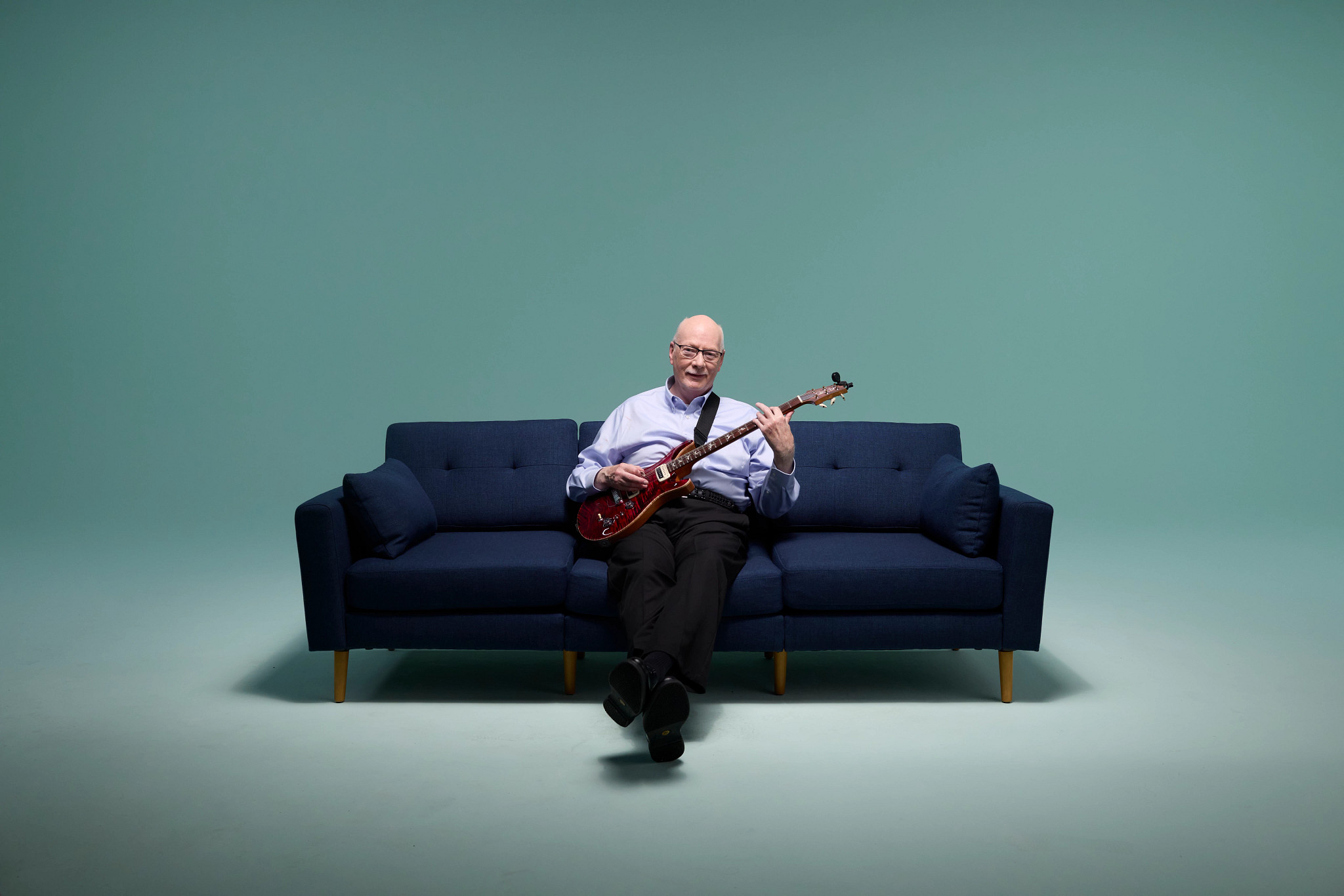 Navy couch on mint background with patient Peter and his guitar.