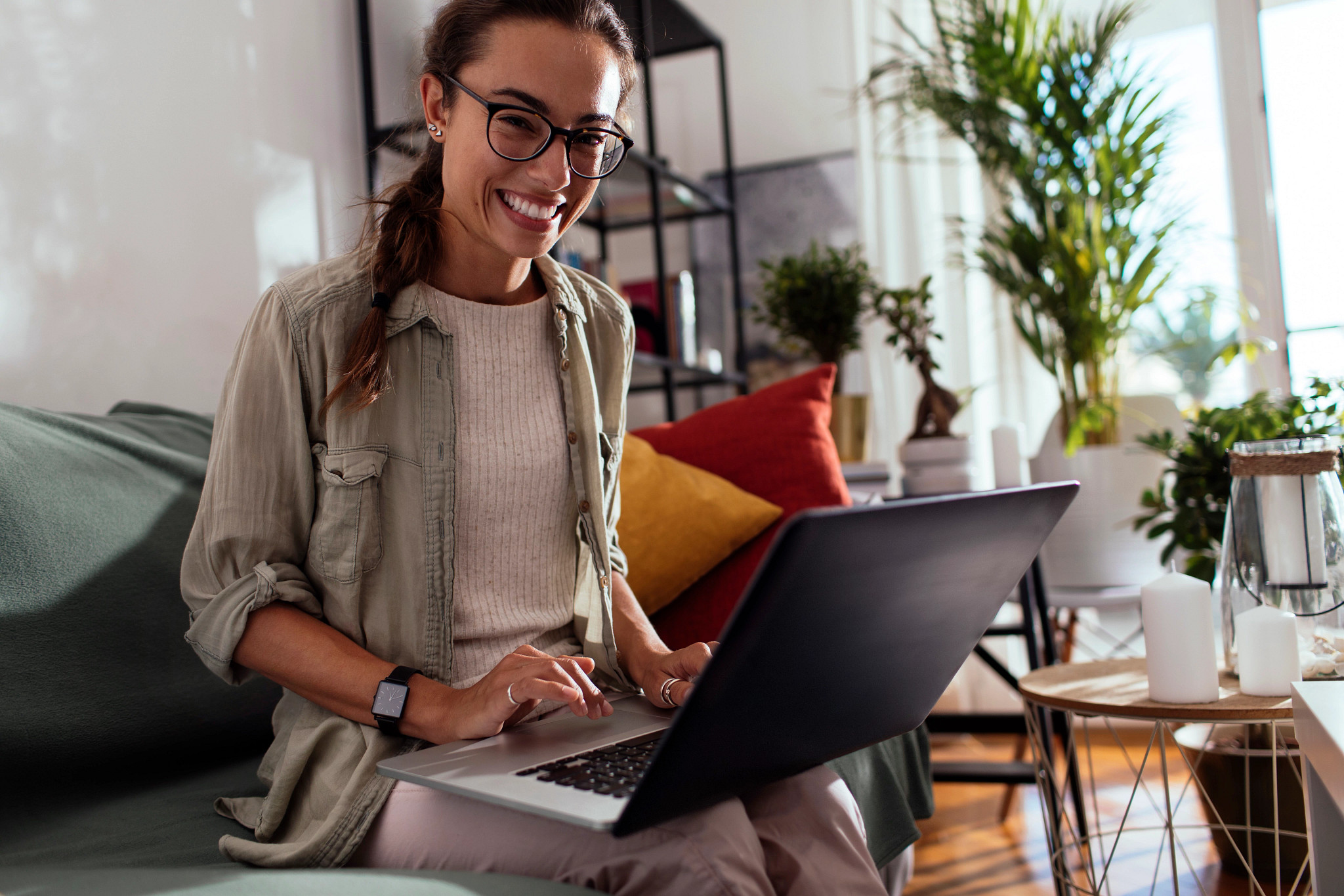 Young woman wearing glasses seated on couch and holding a laptop.