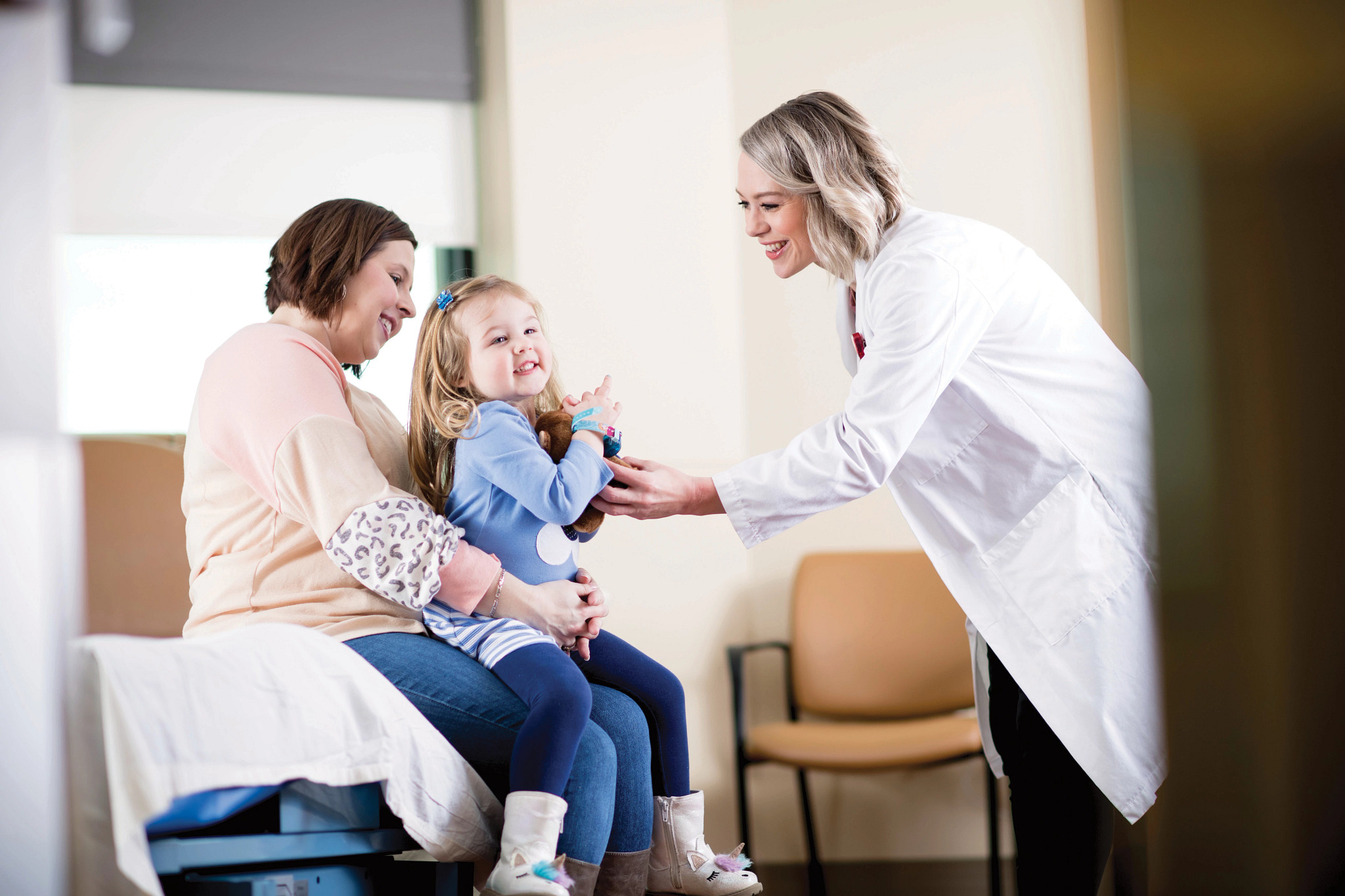 Certified nurse midwife with young patient and mother in exam room.