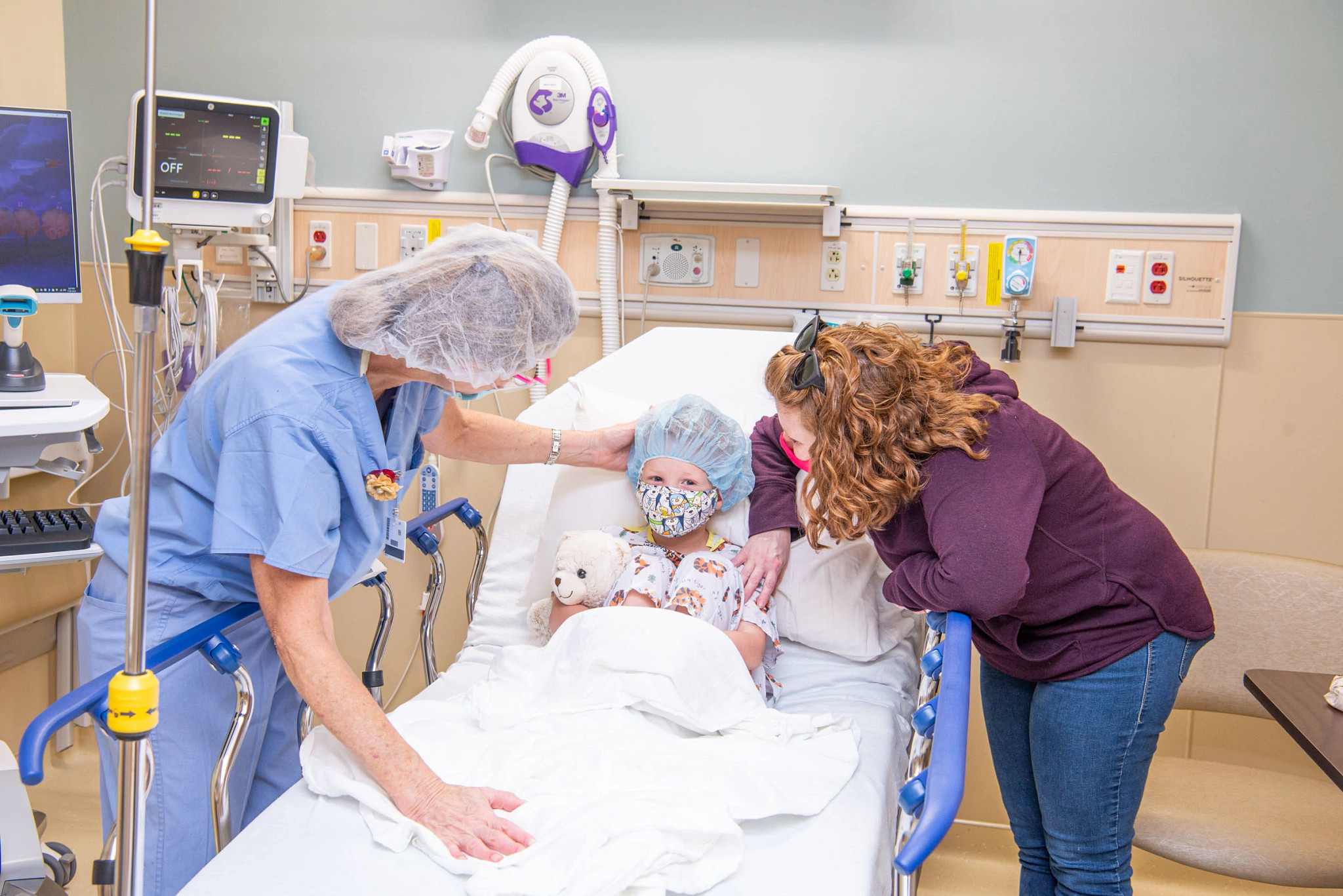 Nurse and mother comforting son at bedside before surgery.