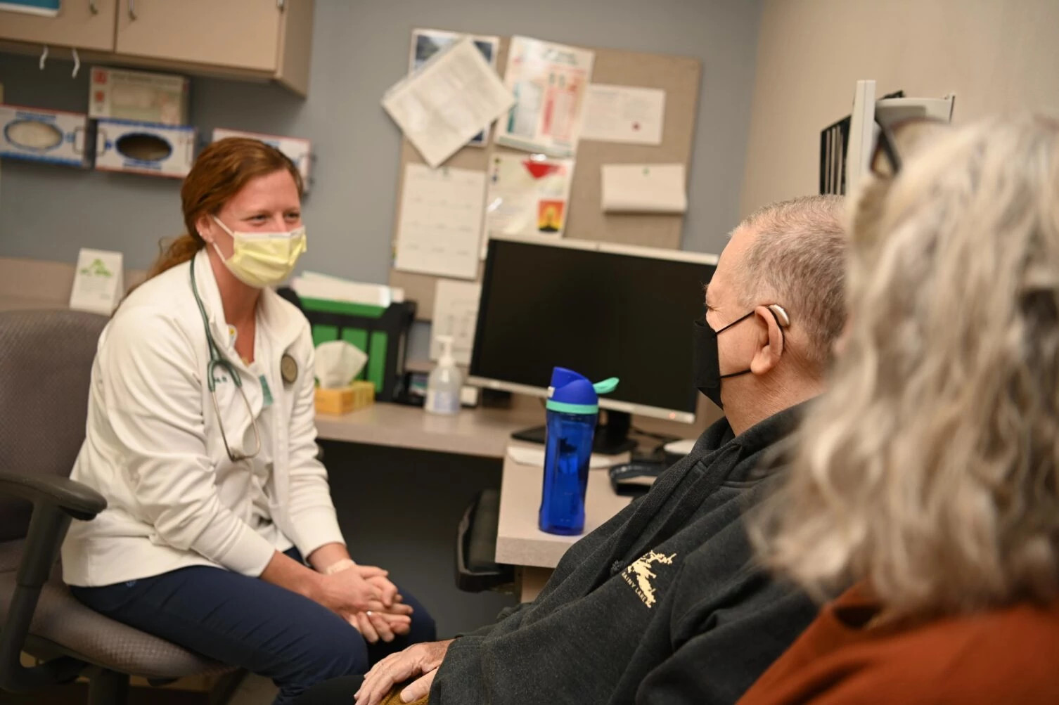 Nurse wearing mask meeting with patients in exam room.