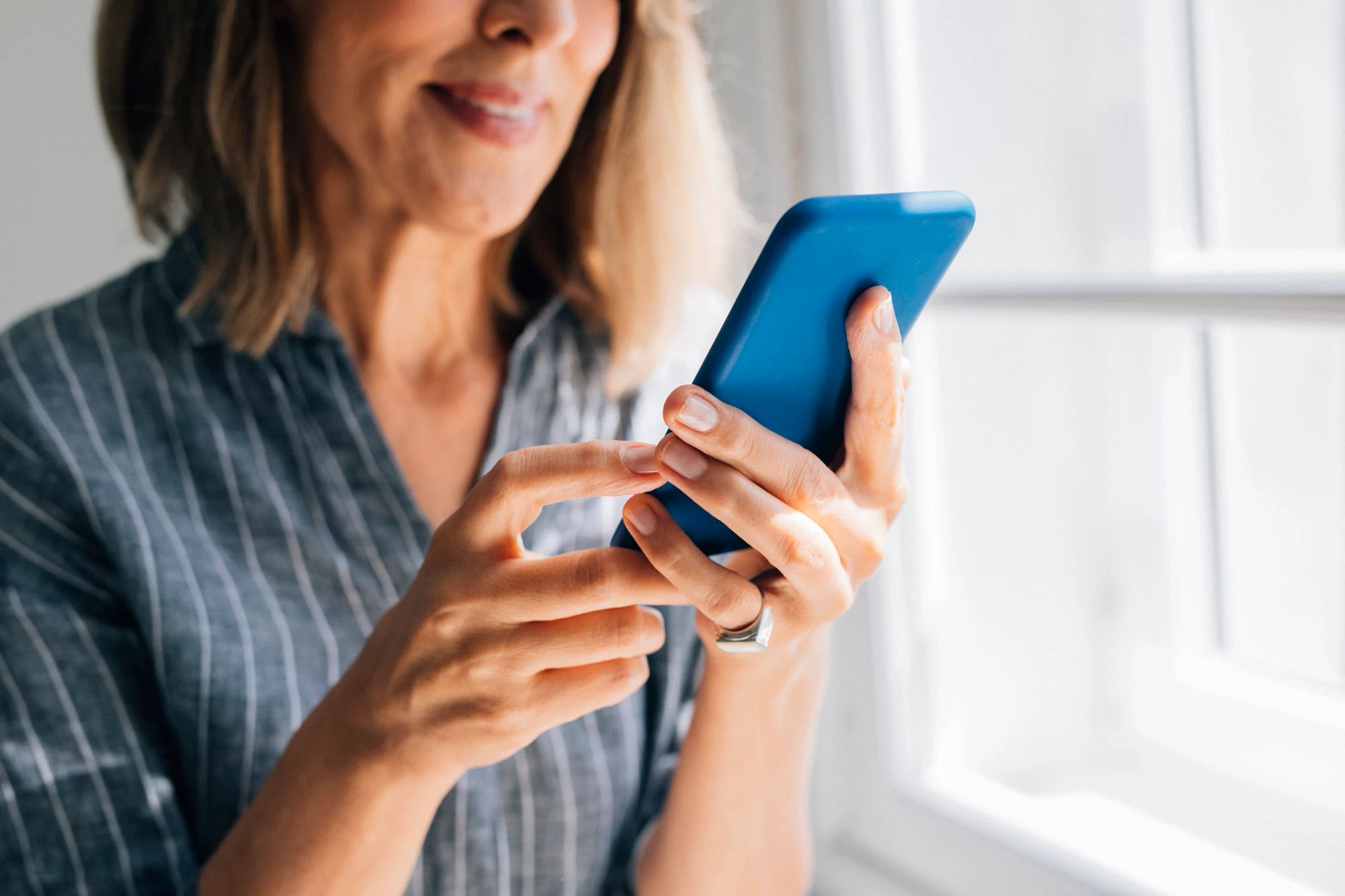 Smiling woman holding a cell phone in her home.