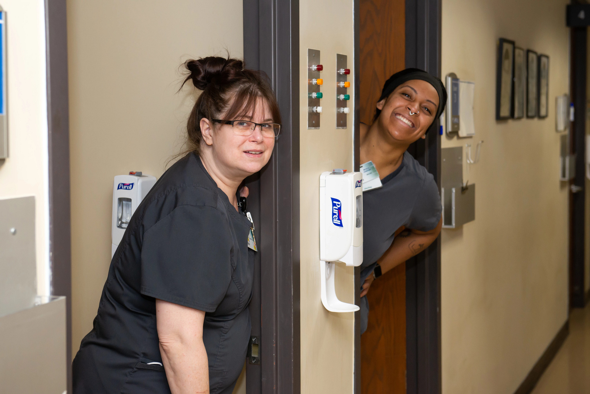 two-medical-assistants-peeking-out-of-adjacent-exam-rooms.jpg