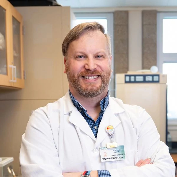 Gundersen Research breast cancer research Kristopher Lofgren wearing white coat in science lab.