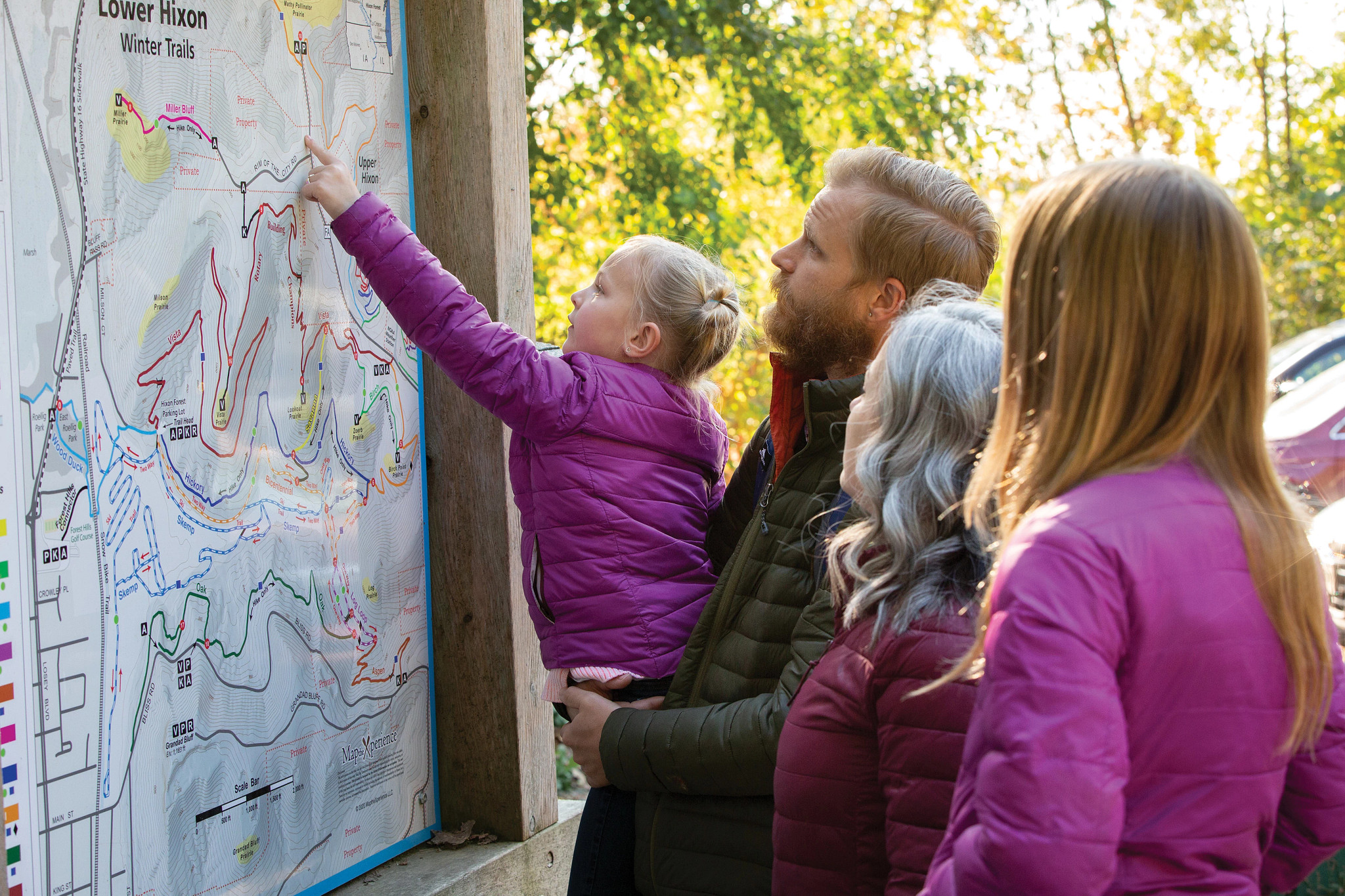 Family of four looking at hiking trails map in autumn.