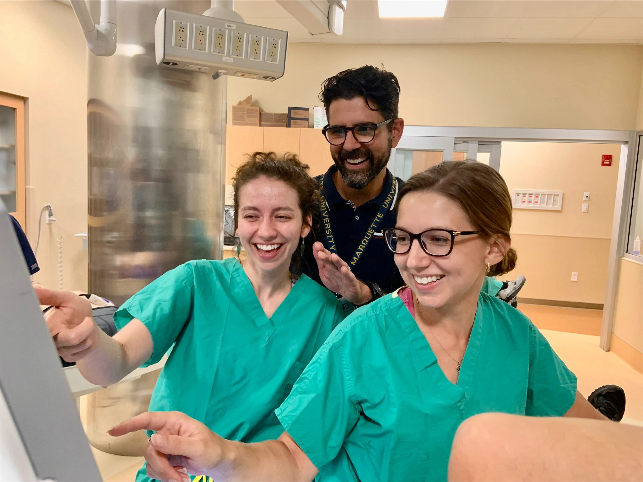 Medical students smiling during patient exam in simulation lab.