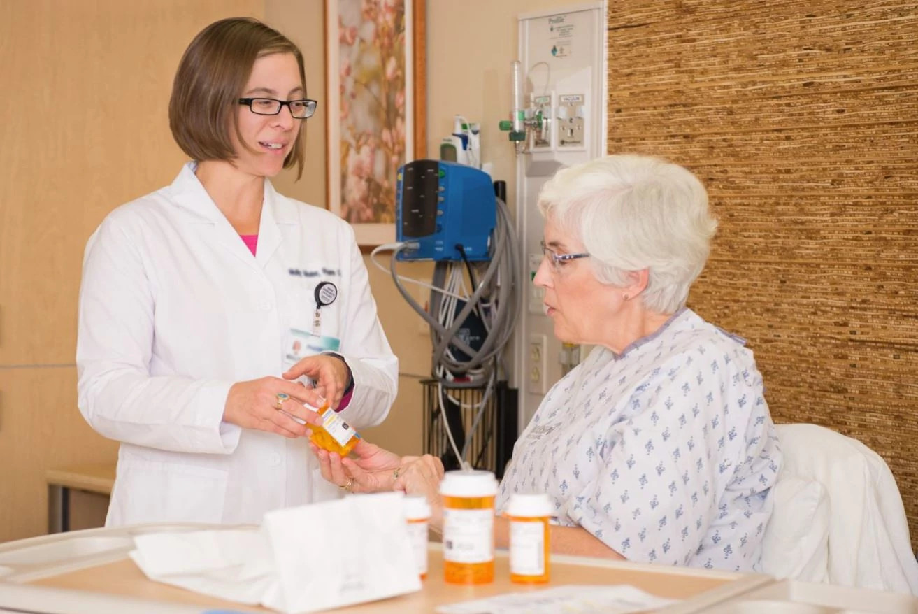 Pharmacist delivering medication to patient in patient room.