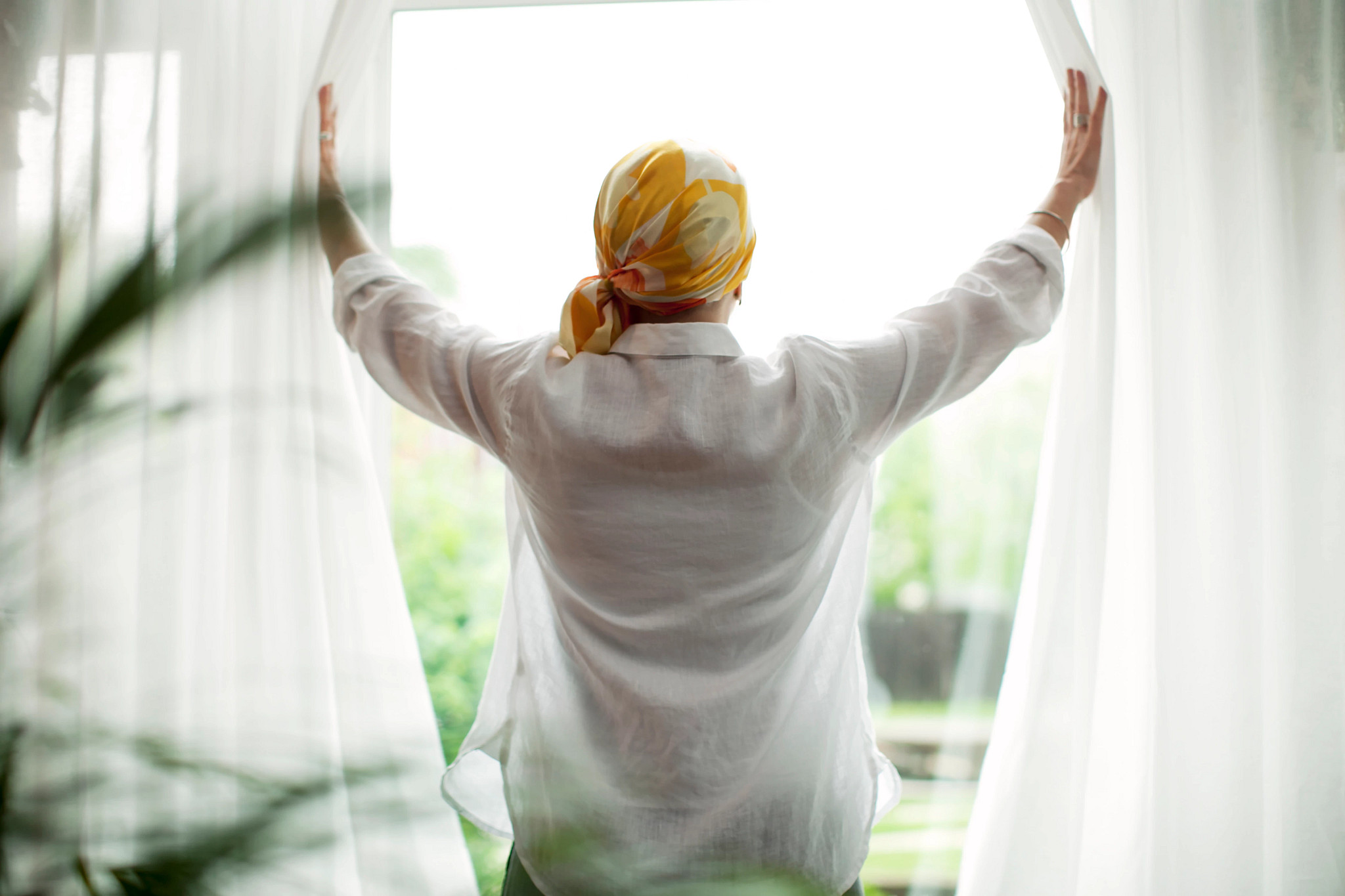 Rear view of mature woman opening curtains at window