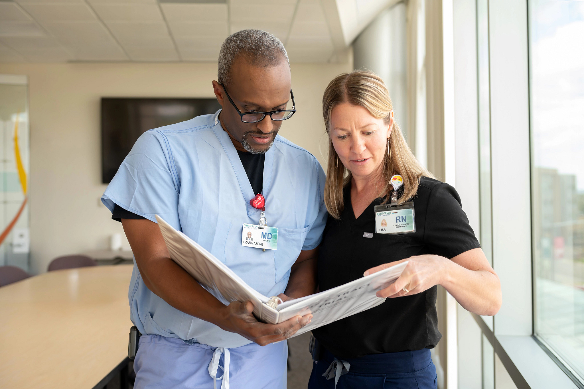 Gundersen clinical trial researchers Ezana Azene, MD, and Lisa Weinberger, RN, reviewing papers in file dressed in scrubs..jpg