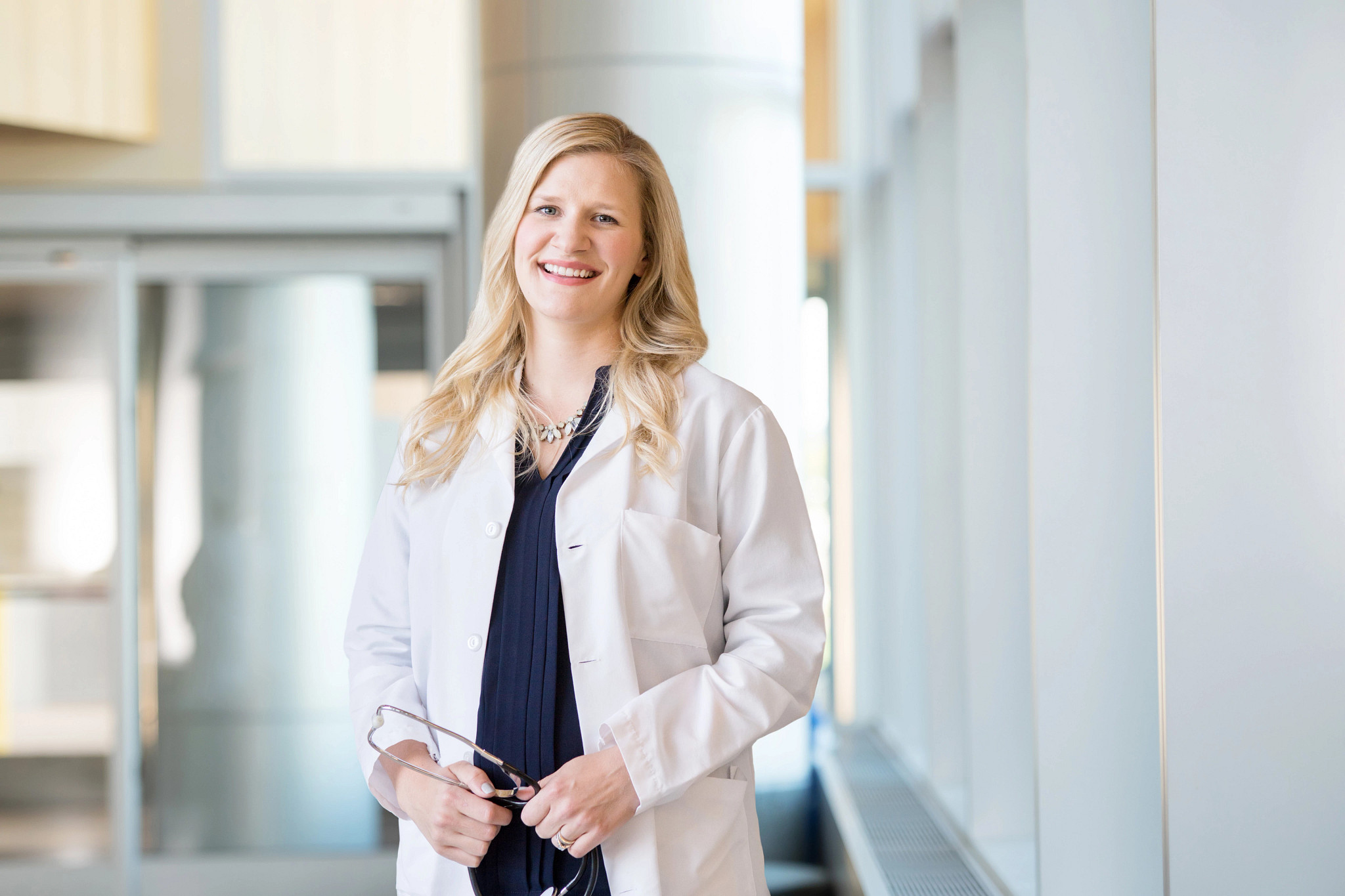 Female doctor smiling in bright hospital hallway.