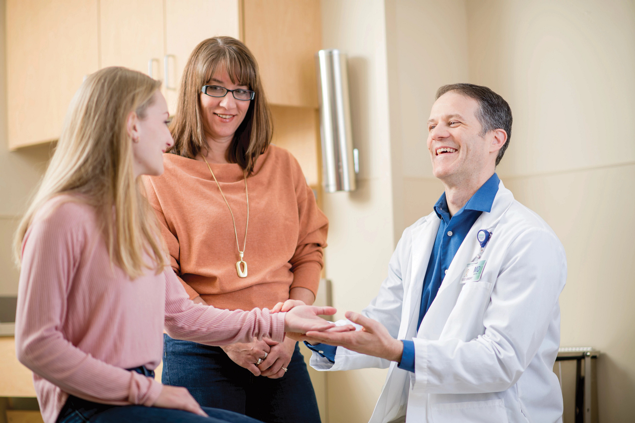 Male doctor giving exam to teenage girl patient while mother looks on.
