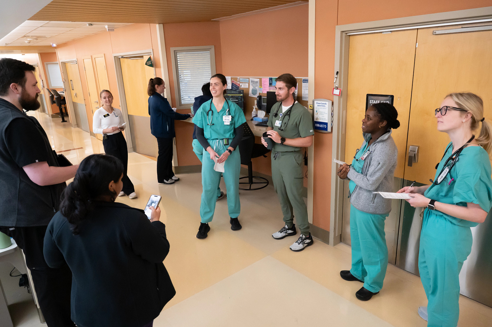 Internal Medicine residents on rounds in hospital unit hallway.
