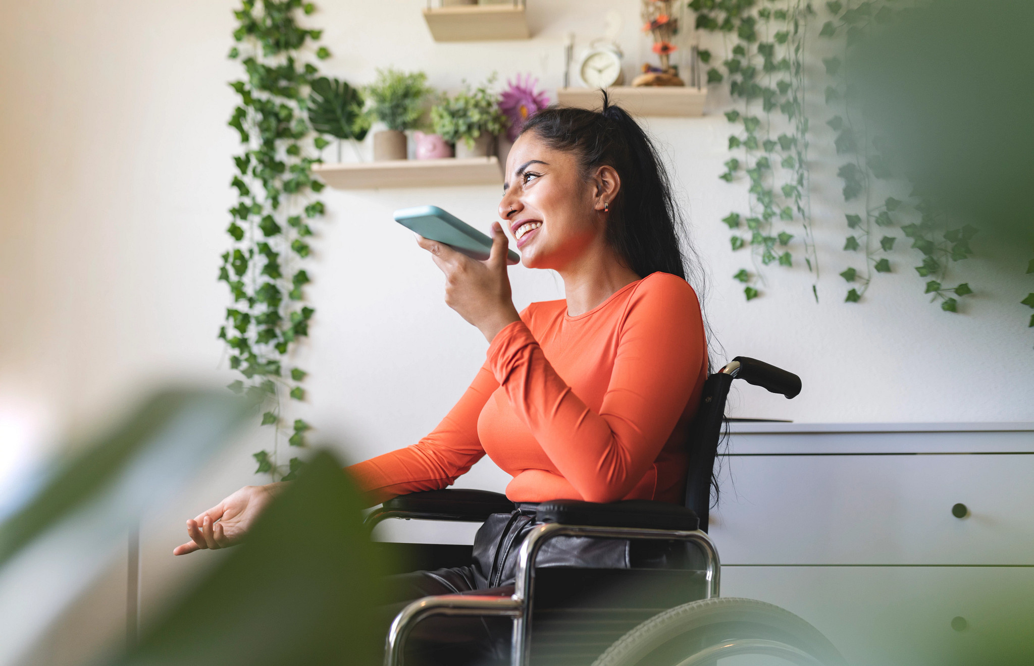 Smiling disabled woman in wheelchair, talking on mobile phone at home.