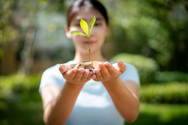 Woman holding sapling with coins in the palm of her hands.