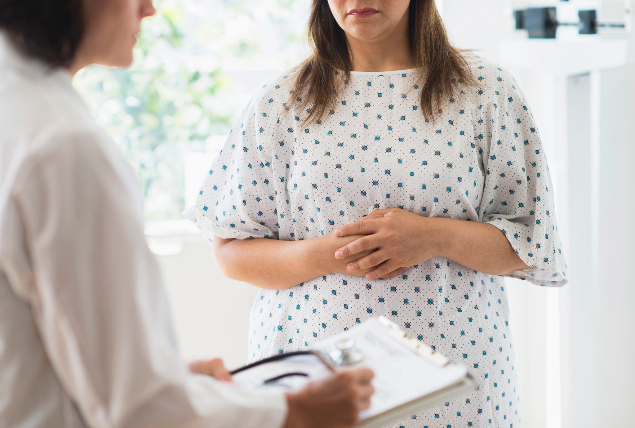 Woman holding stomach in doctors office with doctor doing health checkup.