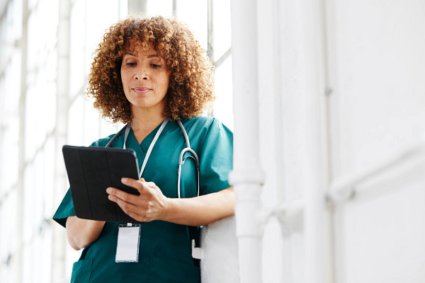 Female healthcare professional looking at digital tablet leaning against window.