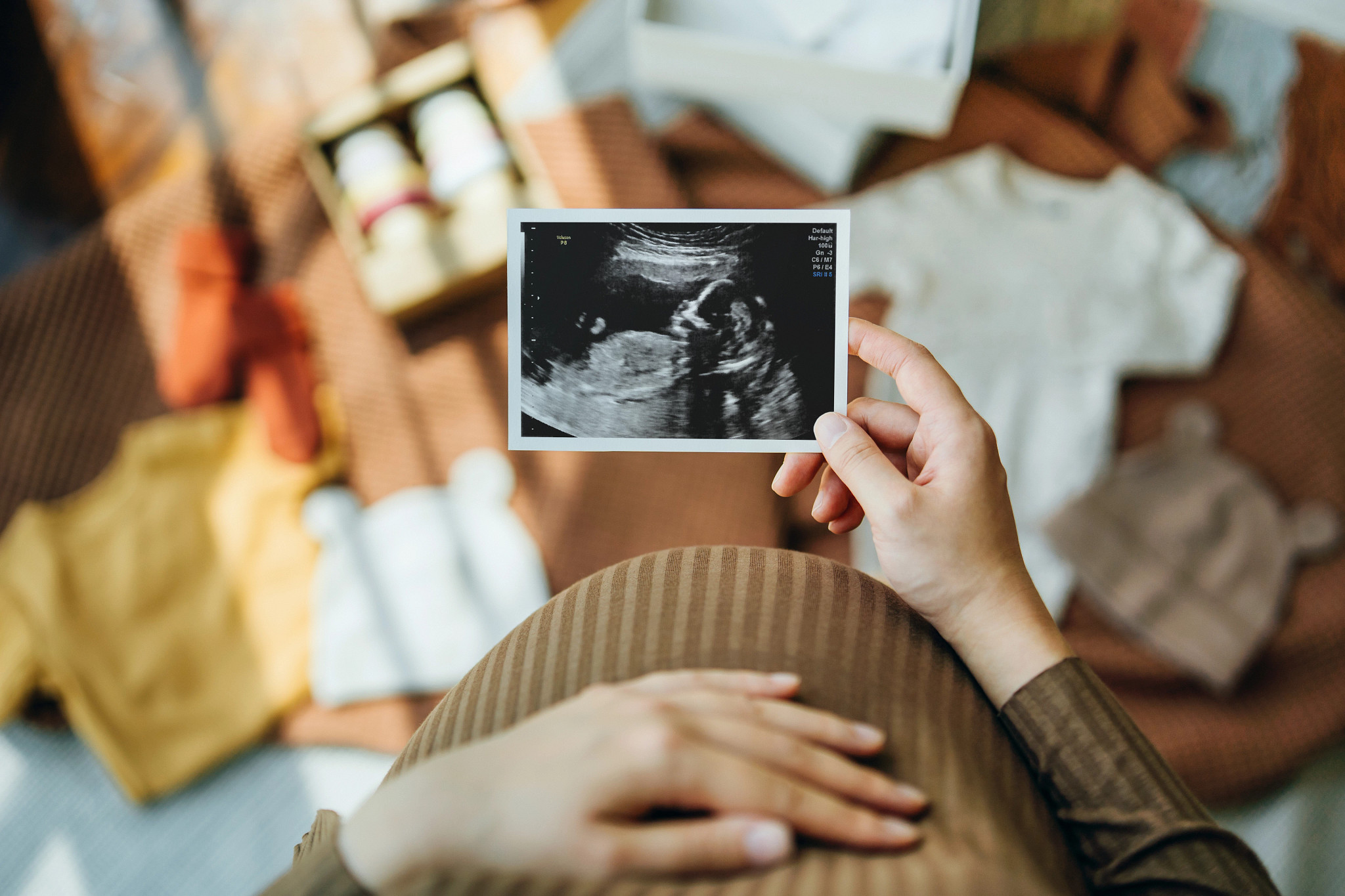 Pregnant woman looking at an ultrasound scan photo while gently touching her baby bump.