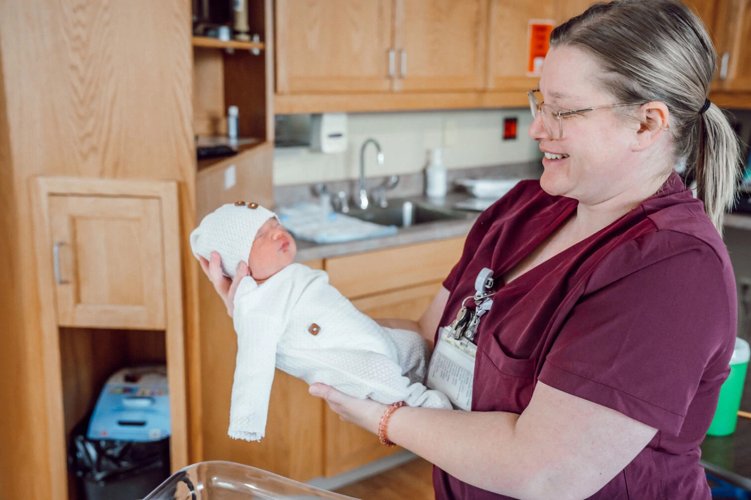 Nurse holding newborn in hospital room.