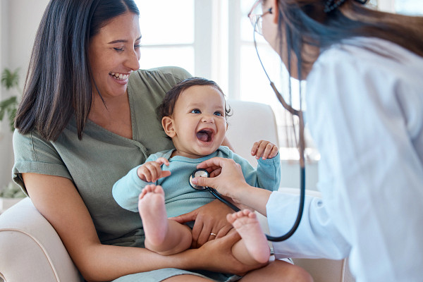 Baby sitting on mother's lap being examined by doctor