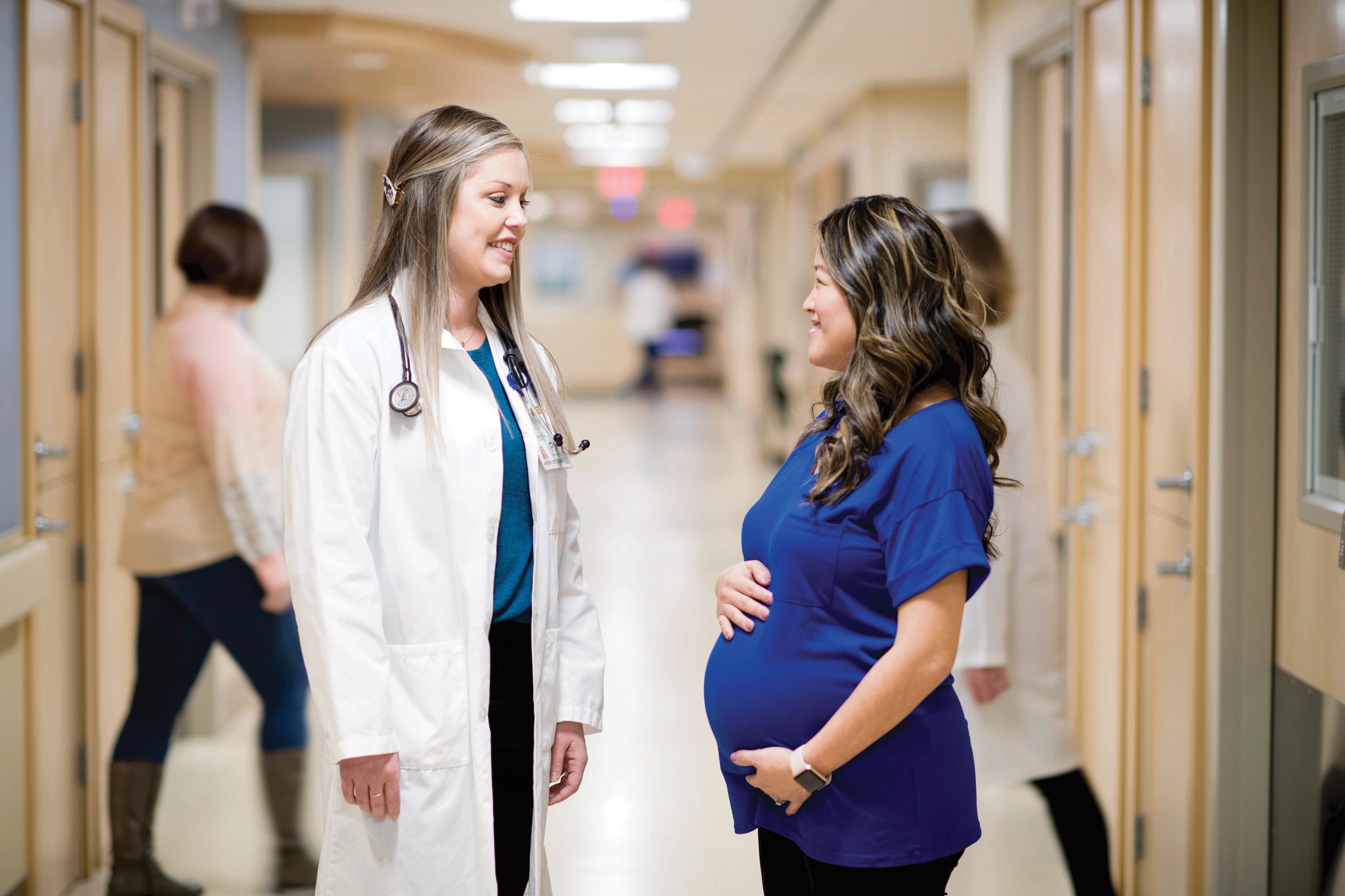 Emplify Health provider Andrea Dietzenbach speaking with pregnant woman in clinic hallway.
